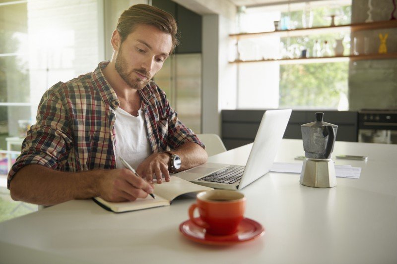 Cropped shot of a handsome young man writing in his journal while using a laptop